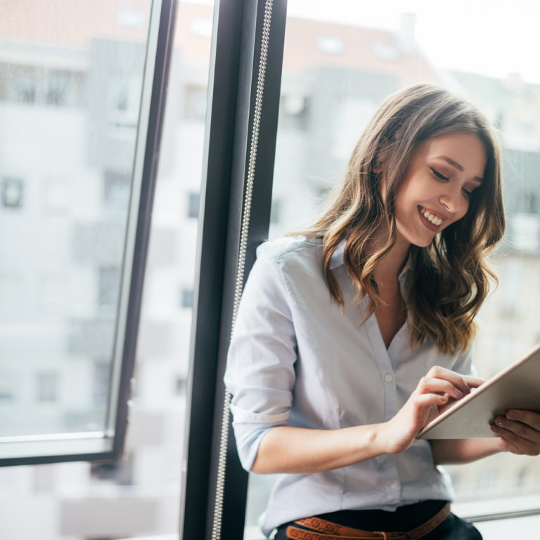 Young businesswoman using a digital tablet while standing in front of windows in office
